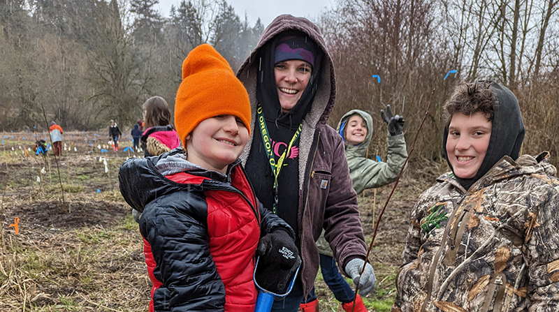 teacher and two students smile, planting trees along Burnt Bridge Creek